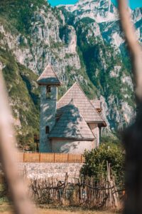 Ein Blick auf eine kleine idyllische Kirche, im Hintergrund die zerklüfteten Berge der albanischen Alpen